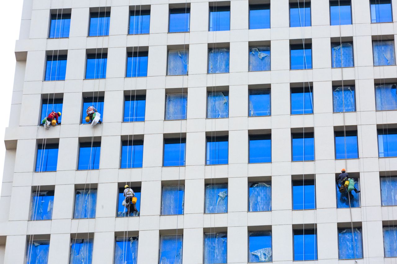 Des ouvriers professionnels nettoient les vitres d’un gratte-ciel à l’aide de cordes, en milieu urbain.